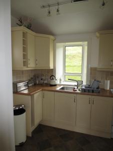 uma cozinha com armários brancos, um lavatório e uma janela em Harris White Cottage em Rodel