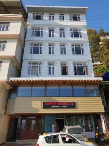 ein weißes Gebäude mit davor geparkten Autos in der Unterkunft Juniper Residency Hotel in Namchi
