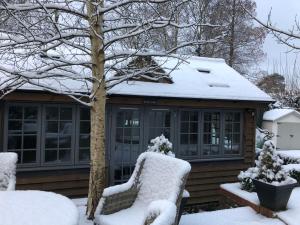 a house covered in snow with two chairs at Truffle Lodge in Lindfield