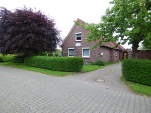 a brick house with hedges in front of a driveway at Ferienwohnung Hanne in Berumbur