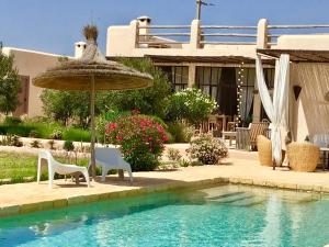 a patio with an umbrella and chairs and a pool at Dar Alya Essaouira Maison et table d'hôtes in Ghazoua