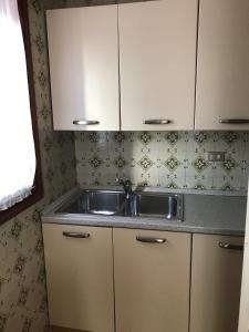una cucina con lavandino e armadietti bianchi di ARISTON - WALTERIGATO Apartments SOLO PER FAMIGLIE a Lido di Jesolo