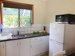 a kitchen with a sink, microwave and refrigerator at Paradise Court Holiday Units in Airlie Beach