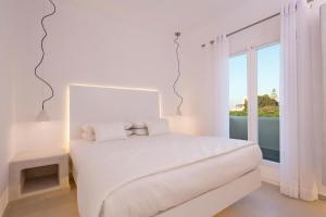 a white bedroom with a white bed and a window at Art Hotel Santorini in Pyrgos