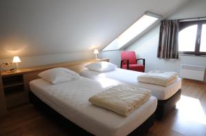 two beds in a hotel room with a red chair at La Coline in Somme-Leuze