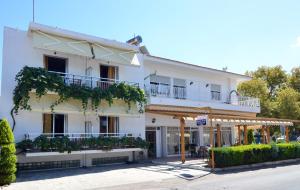 a white building with balconies and trees on a street at Polizotou Rooms in Skala Sotiros