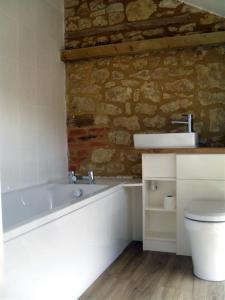 a bathroom with a white tub and a stone wall at Toad Hall at Tove Valley Cottages in Towcester