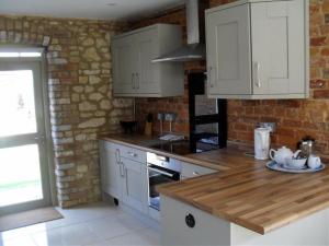 eine Küche mit weißen Schränken und einer Ziegelwand in der Unterkunft Toad Hall at Tove Valley Cottages in Towcester + 5 Fotos
