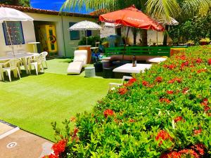 - un jardin avec des tables, des chaises et des fleurs rouges dans l'établissement Ótima Localização casa, 7 quartos-Porto de Galinhas 900m piscinas naturais, à Porto de Galinhas