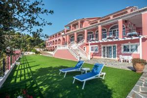 two blue chairs on a lawn in front of a pink building at Hotel Elena Ermones in Ermones