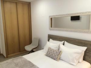 a bedroom with a bed with a chair and a mirror at Casinha do Rossio in Aveiro