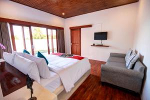 a bedroom with a bed and a chair and a television at Prawiba Villa in Keramas