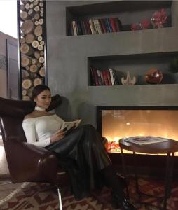 a woman sitting in a chair reading a book next to a fireplace at Bugu Hotel Bishkek in Bishkek