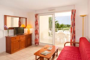 a living room with a red couch and a tv at Vacancéole - Résidence Le Palmyra Golf in Cap d'Agde