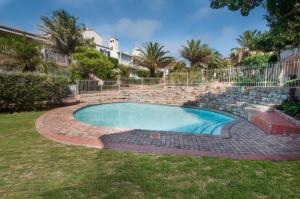 a swimming pool in a yard with a stone retaining wall and trees at Port Main Royal Ocean's Edge in St Francis Bay