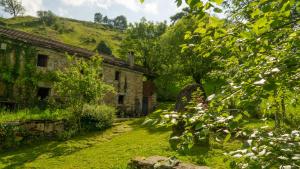 un vieux bâtiment en pierre et une cour avec de l'herbe et des arbres dans l'établissement Cabaña en las montañas, à San Roque de Ríomiera