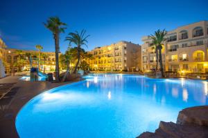 a large swimming pool with palm trees and buildings at Grupotel Alcudia Pins in Playa de Muro