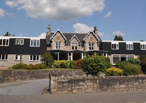 a large black and white house with a stone wall at The Acarsaid - Pitlochry in Pitlochry