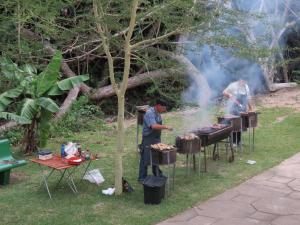 a man cooking food on a grill in the grass at Dieu Donnee River Lodge in Port Shepstone
