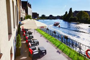 eine Reihe von Stühlen und ein Regenschirm neben einem Fluss in der Unterkunft Qubus Hotel Gdańsk in Danzig