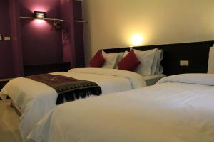 a bedroom with two beds with white sheets and red pillows at Sri Chumphon Hotel in Chumphon