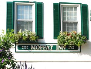 a sign on a building with two windows and flowers at Moffat Inn in Niagara-on-the-Lake