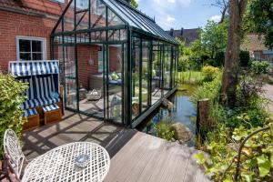 a glass greenhouse on a deck next to a pond at Landhaus Alte Apotheke in Großefehn 