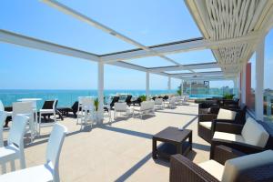 eine Terrasse mit weißen Stühlen, Tischen und Meerblick in der Unterkunft Grande Albergo Marin in Lignano Sabbiadoro