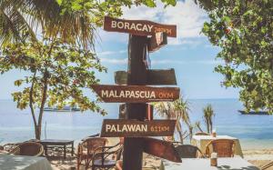 um poste com placas de rua na praia em Hippocampus Beach Resort em Malapascua Island