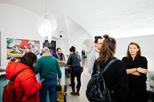 un groupe de personnes se tenant dans une exposition d'art dans l'établissement Long Story Short Hostel & Café, à Olomouc