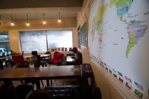 Kimchee Haeundae Guesthouse في بوسان: شخص يجلس على طاولة في غرفة مع خريطة على الحائط