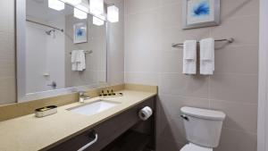 a bathroom with a toilet, sink, and mirror at Best Western Plus Stadium Inn in Bronx