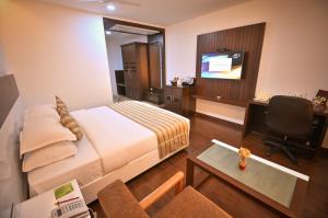 ein Hotelzimmer mit einem Bett, einem Schreibtisch und einem TV in der Unterkunft Chola Serviced Apartment in Tiruchchirāppalli