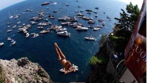 a group of boats in a harbor with a man jumping off a cliff at Villamena in Furore