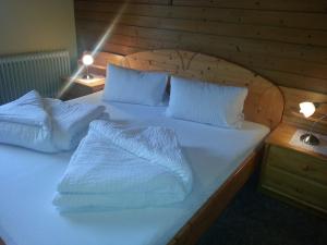 Cama con cabecero de madera con sábanas y almohadas blancas en Haus Karwendelblick, en Leutasch