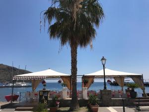 利帕里的住宿－Deluxe Lipari Room，棕榈树,坐在海滩旁,摆放着桌子和遮阳伞