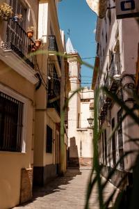 eine schmale Gasse mit Gebäuden und einem Uhrturm in der Unterkunft La Judería del Buen Viaje in Sevilla