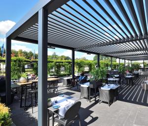 une terrasse avec des tables, des chaises et des auvents. dans l'établissement Van Der Valk Hotel Brugge Oostkamp, à Oostkamp