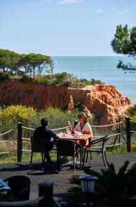 a man and woman sitting at a table near the ocean at PortoBay Falesia in Albufeira