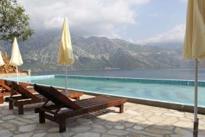 ein Pool mit zwei Bänken und Sonnenschirmen in der Unterkunft Boka Gardens Seaside Resort in Kotor