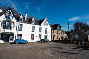 un edificio blanco con dos coches estacionados frente a él en The Kirkmichael Hotel, en Kirkmichael