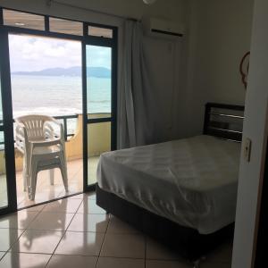 een slaapkamer met een bed en een stoel en de oceaan bij Apartamento a Beira Mar in Meia Praia