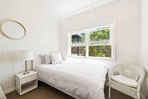 a white bedroom with a bed and a chair and a mirror at Hollow Tree Farm in Toowoomba