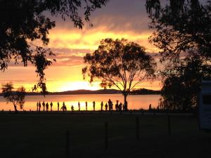 un grupo de personas de pie frente a un lago al atardecer en Lake Hume Holiday Park en Lake Hume