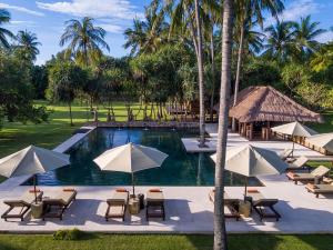 a resort pool with chairs and umbrellas and palm trees at Sira Beach House in Tanjung