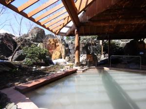 a swimming pool with a wooden roof and some rocks at Hotel Sunvalley Nasu in Nasu
