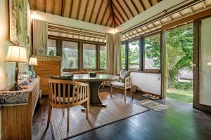 ein Wohnzimmer mit einem Tisch, Stühlen und Fenstern in der Unterkunft Villa Umah Shanti in Ubud