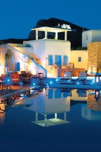 a pool of water with chairs and buildings at night at Chora Resort Hotel & Spa in Chora Folegandros