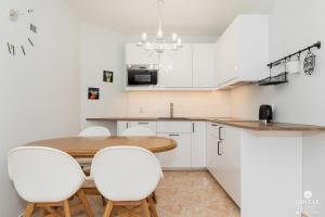 a kitchen with a wooden table and white chairs at Jantar Apartamenty - Park Side in Kołobrzeg