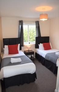 1 dormitorio con 2 camas con almohadas rojas y ventana en Kelpies Serviced Apartments Alexander- 2 Bedrooms, en Falkirk